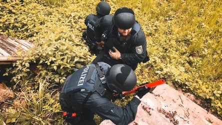 Drei Polizisten hocken auf einer Wiese