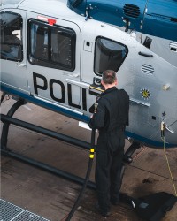 Bildausschnitt: Ein Kollege steht am hinteren Teil des Hubschraubers und befüllt ihn mit dem Tankschlauch.