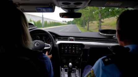 Eine Polizistin am Steuer und ein Polizist als Beifahrer im Polizeiauto. In der Mitte zwischen ihnen ist das „Infotainment-System Polizei“ (ISP).