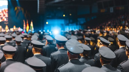 Vereidigung in der Ausbildung oder im Studium: Das Foto zeigt mehrere Reihen an Polizei-Anwärterinnen und -Anwärtern in Uniform und Mütze. Sie blicken auf die Bühne.