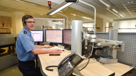 Ein Polizist steht vor seinem Arbeitsplatz in der Notruf-Zentrale der Polizeidirektion Görlitz. Vor ihm sind mehrere Monitore, er trägt ein Headset.